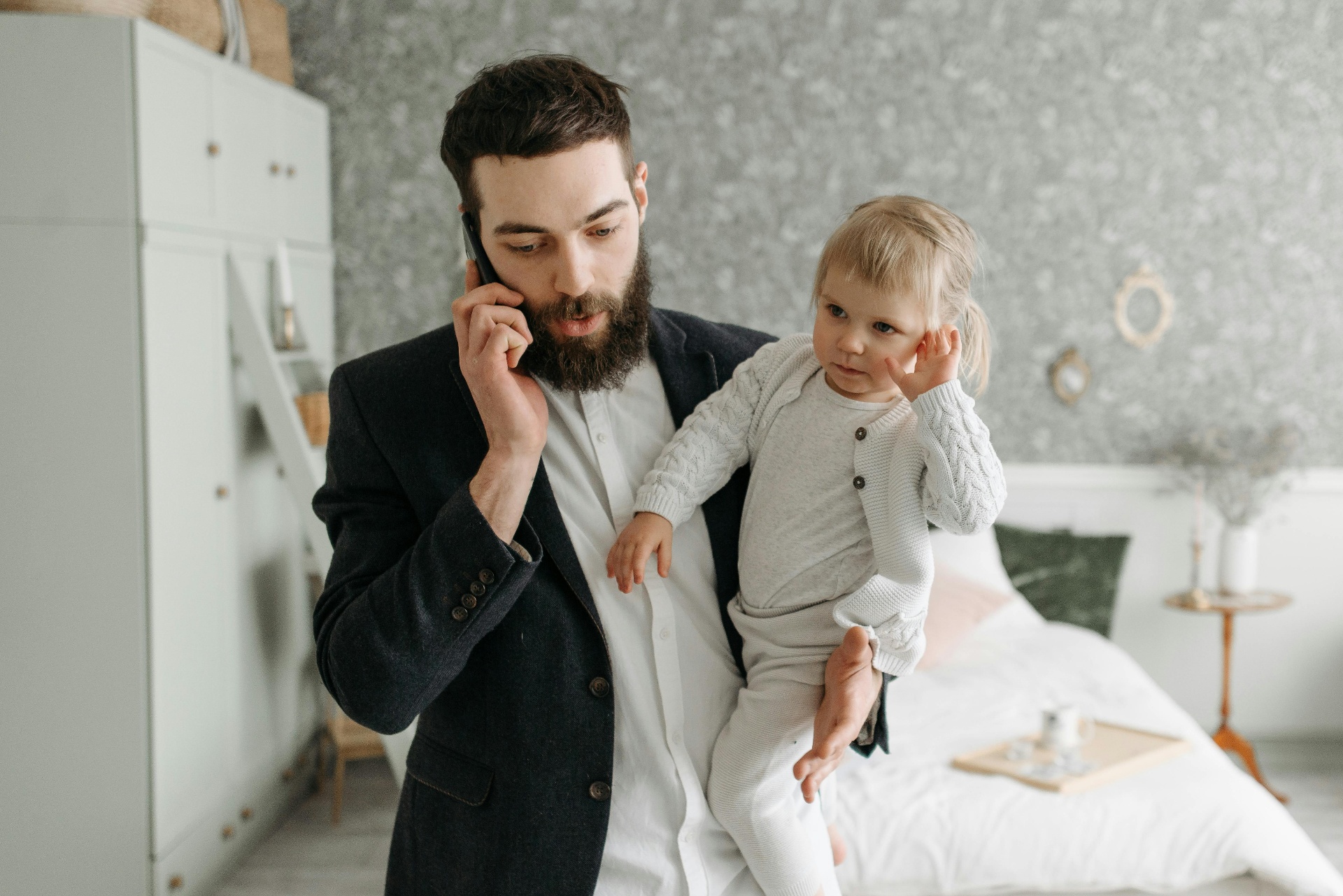A dad holding his toddler while on a phone call at home
