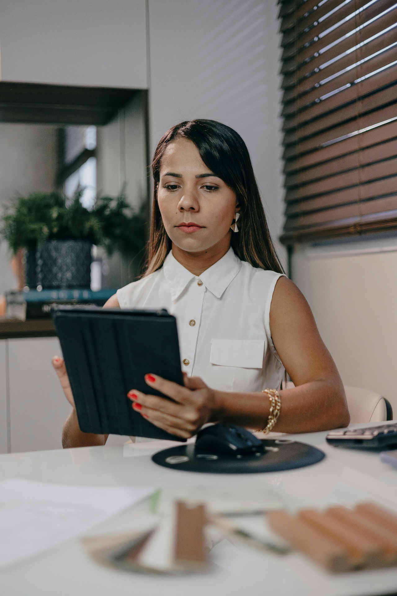 A woman focused on her tablet at a tidy desk by a sunlit window
